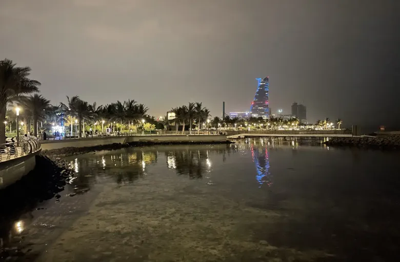 The Jeddah Corniche in Saudi Arabia at night, its promenade and palms lit along the Red Sea waterfront with the city skyline beyond.