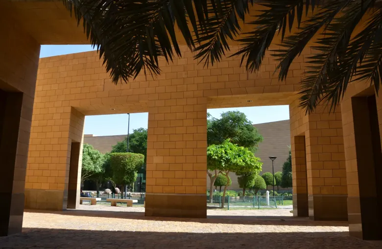 The stone colonnade of the National Museum of Saudi Arabia in Riyadh, framing a garden of palms and shade trees.