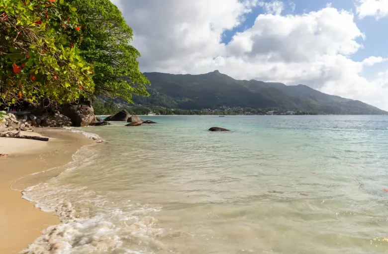 The long sand of Beau Vallon bay on Mahé, calm water and the island's mountain ridge behind.