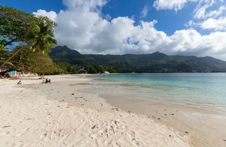 People spread along the sand at Beau Vallon on Mahé, the bay opening out beyond the treeline.