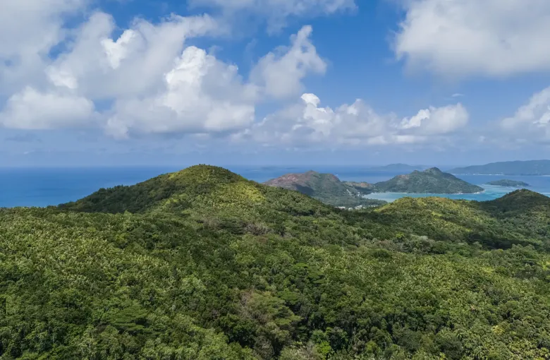 Green forested hills on Praslin falling away towards the sea, with further granitic islands on the horizon.