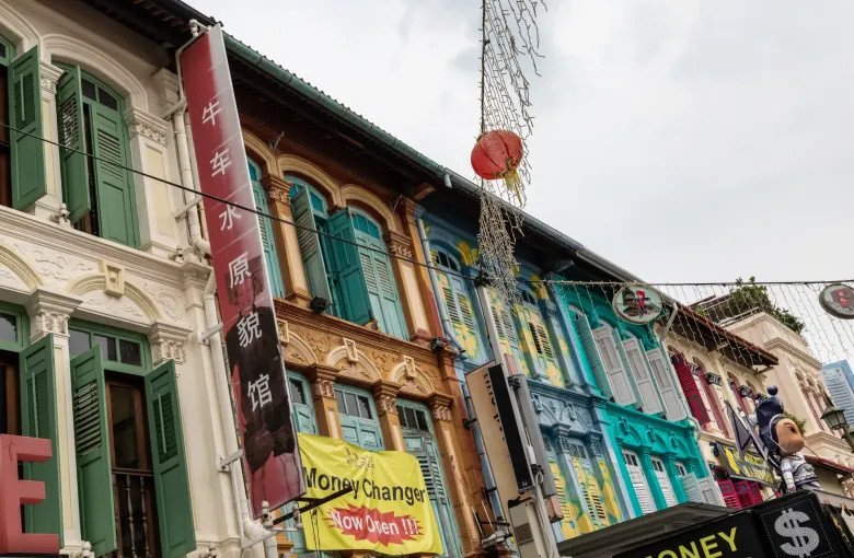 Shophouse upper floors on Pagoda Street in Singapore's Chinatown, above a money changer's board and a lit dollar sign.