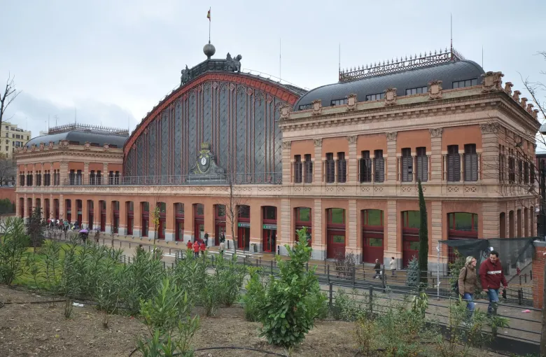 The brick and iron front of Atocha railway station in Madrid, Spain, its arched train shed roof behind a clock.