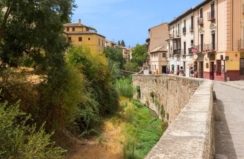 The cobbled Carrera del Darro climbing beside a stone parapet above the Darro riverbed in Granada, Spain.