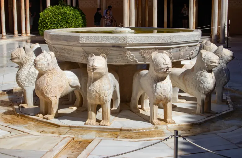 Carved marble lions spouting water beneath the inscribed basin of the lion fountain in the Alhambra at Granada, Spain.