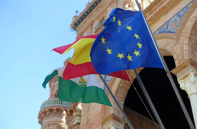 The flags of the European Union, Spain and Andalusia flying against the tiled brickwork of the Plaza de Espana in Seville.