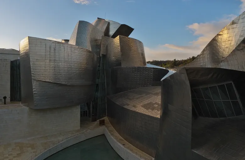 The curved titanium and limestone volumes of the Guggenheim Museum in Bilbao, Spain, in low afternoon sun.