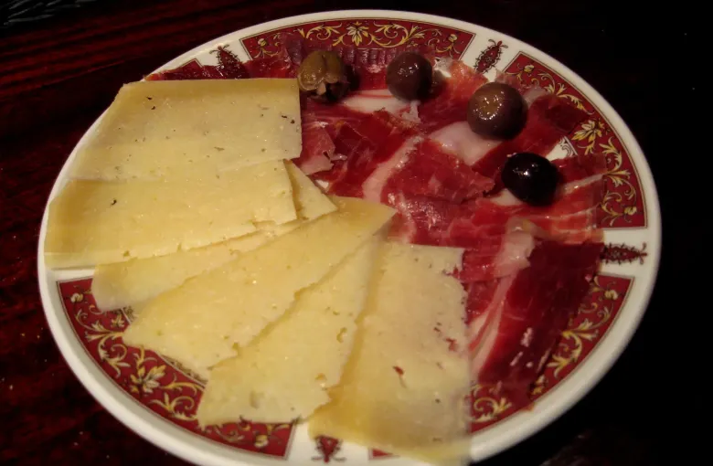 A plate of cured ham slices, wedges of hard cheese and dark olives served as a tapa in Seville, Spain.