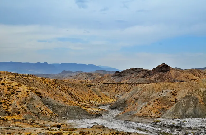 The eroded ochre and gray gullies of the Tabernas desert in Almeria, southeast Spain, with dry scrub and distant ranges.