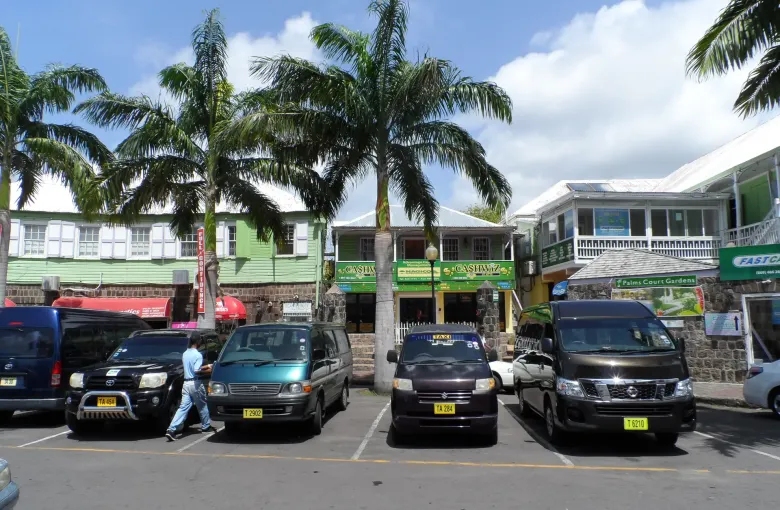 Shopfronts and first-floor verandahs in central Basseterre behind a row of parked minibuses.