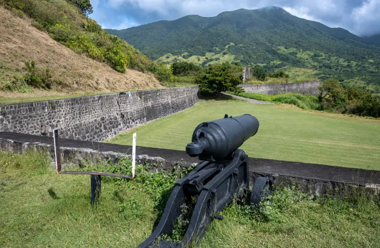 A cannon inside Brimstone Hill Fortress, the stone curtain wall along the parade ground, volcano behind.