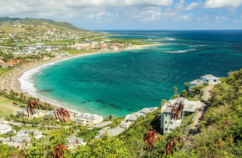 Frigate Bay from a hillside on St Kitts, pale sand and turquoise water inside a reef, green hills behind.