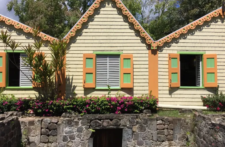 A shingled building at Romney Manor with orange carved fretwork along its gables and green shutters.