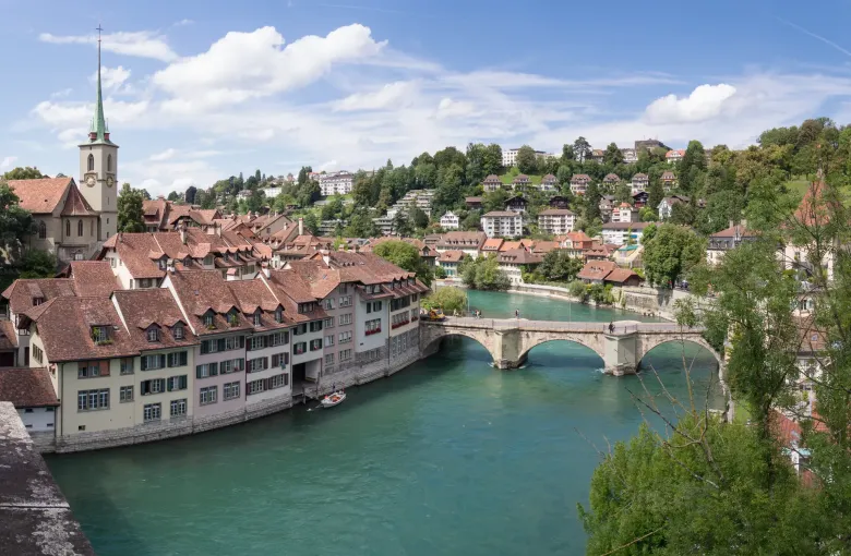 The tiled roofs of Bern's old city packed above the green Aare, with a stone bridge crossing the river below them.