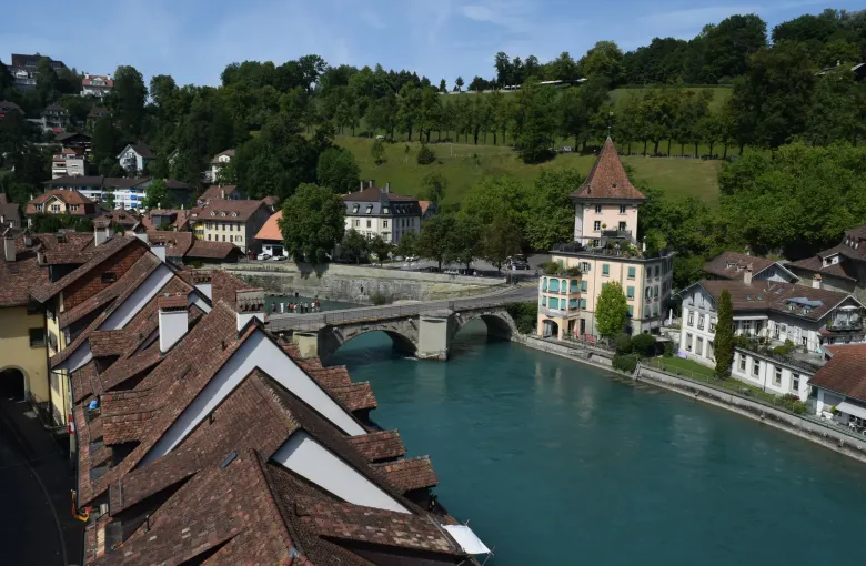 The stepped tile roofs of Bern's old city above the turquoise Aare, with a bridge and a tower on the far bank.