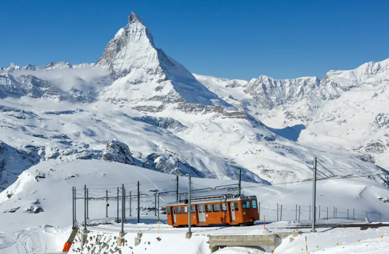 A red Gornergrat railway car standing in deep snow on the open mountainside with the Matterhorn behind it.