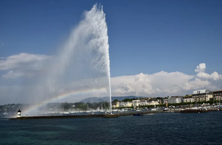 The Jet d'Eau throwing a tall plume of water above Lake Geneva at Geneva, a rainbow forming in the spray.