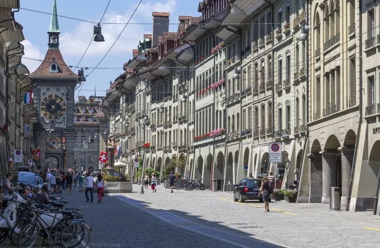 The arcaded shopfronts of the Kramgasse in Bern running down towards the Zytglogge clock tower, flags out above the street.