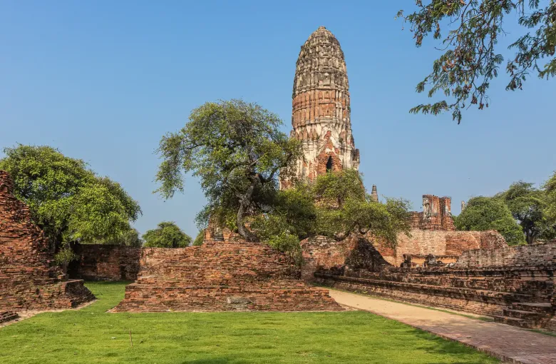 The weathered brick prang of Wat Ratchaburana rising above ruined walls and mown grass at Ayutthaya.