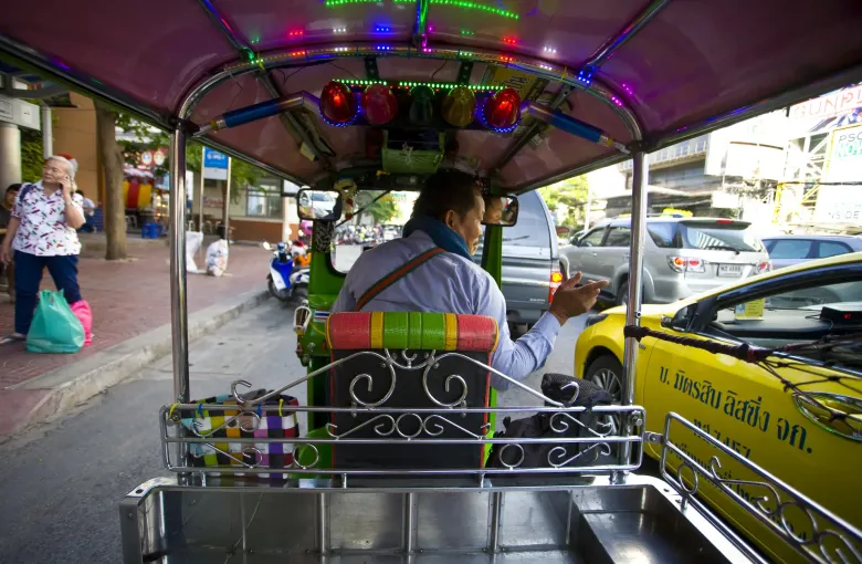 The view forward from the back seat of a tuk-tuk in Bangkok traffic, with taxis alongside and lights overhead.