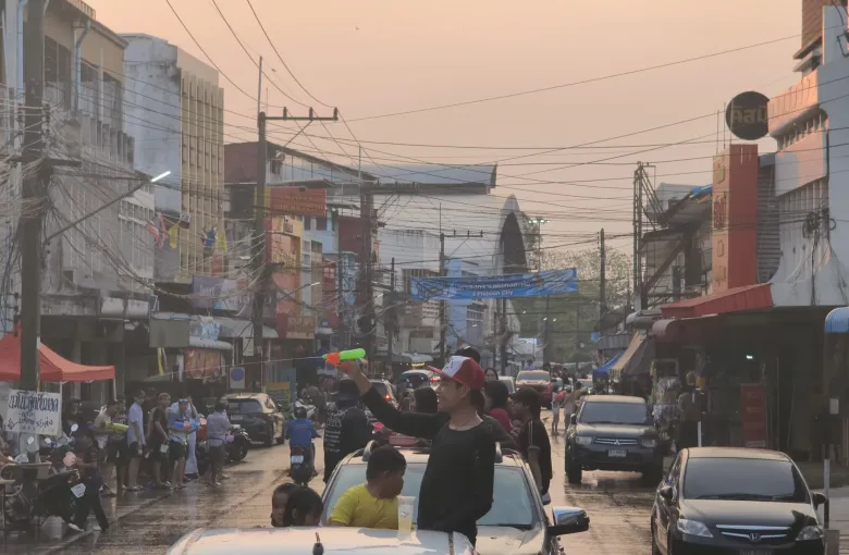 People riding in the backs of pickup trucks along a Thai street during Songkran, water guns in hand.