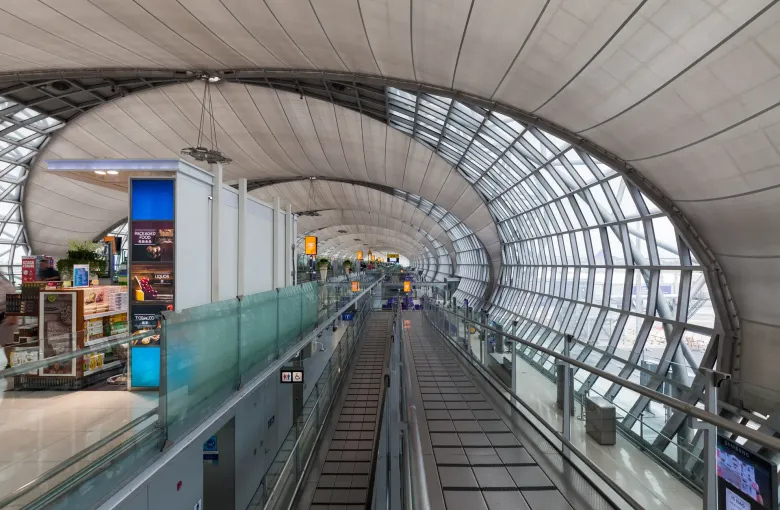 A long glass and steel arrivals concourse at Suvarnabhumi Airport in Bangkok, with travelators along its length.
