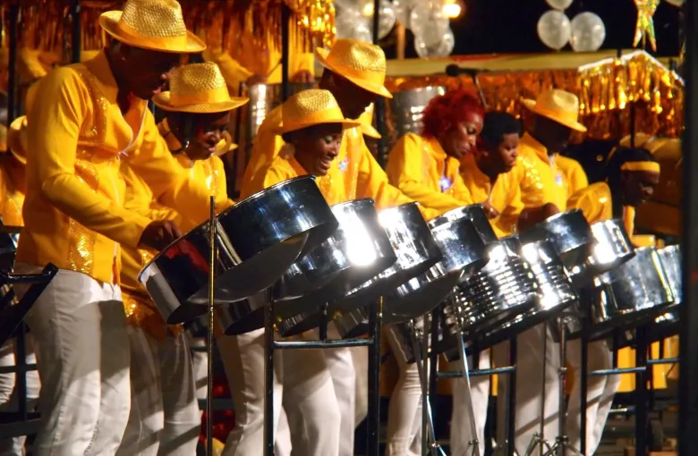 Players in gold shirts and straw hats at their pans in a Trinidad and Tobago steelband during Carnival.
