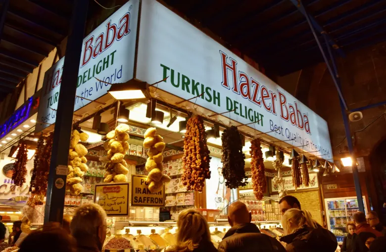 A confectionery stall hung with dried fruit and Turkish delight in the Grand Bazaar in Istanbul, Turkey, with shoppers at the counter.