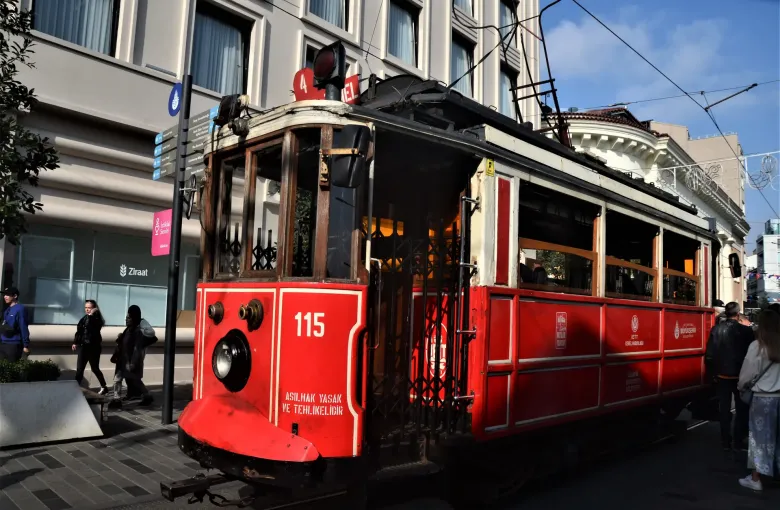 The red nostalgic tram on Istiklal Avenue in Istanbul, Turkey, with pedestrians alongside it on the shopping street.