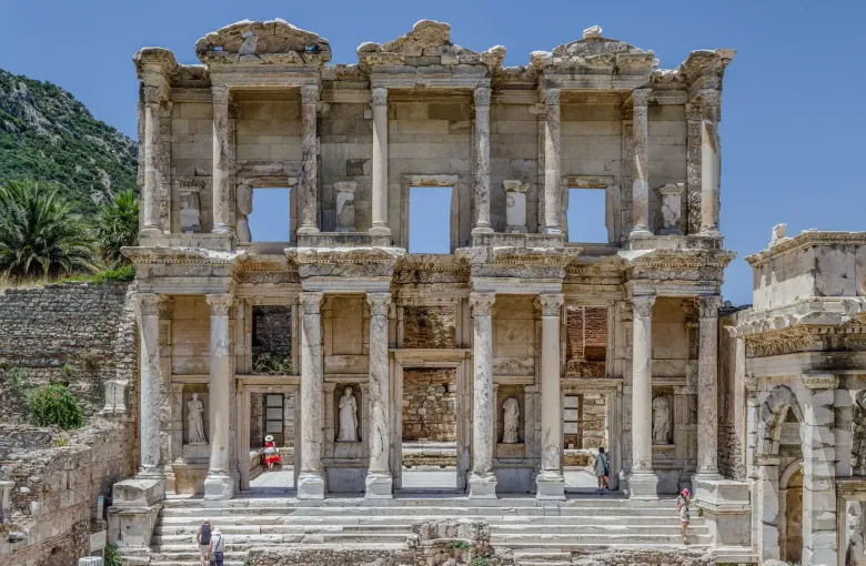 The two-storey marble facade of the Library of Celsus at Ephesus in Turkey, its columns and statue niches standing against a wooded hillside.