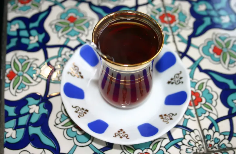 A tulip glass of Turkish tea on a saucer set on a blue and white Iznik-patterned tile.