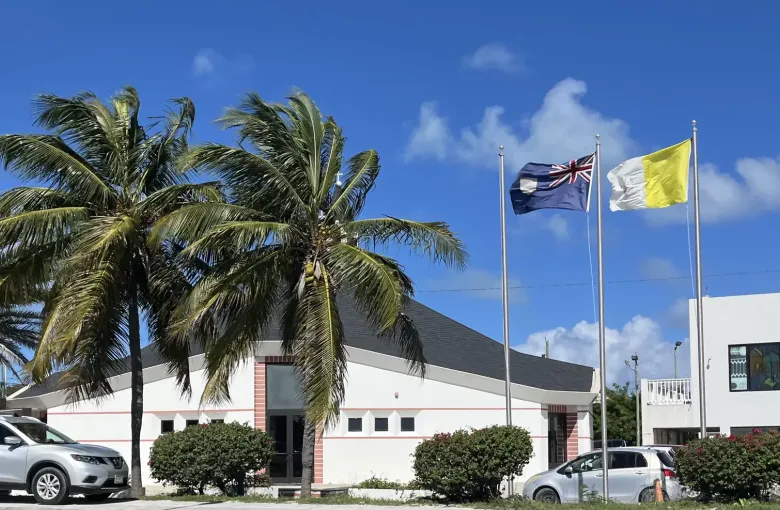 A white church on Providenciales behind palms, with the territory flag and a second flag flying on tall poles.