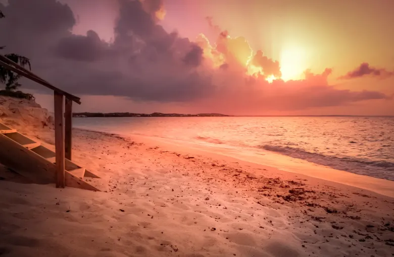 Pink and gold cloud at sunset over the beach at Grace Bay, with a weathered wooden stairway down to the sand.
