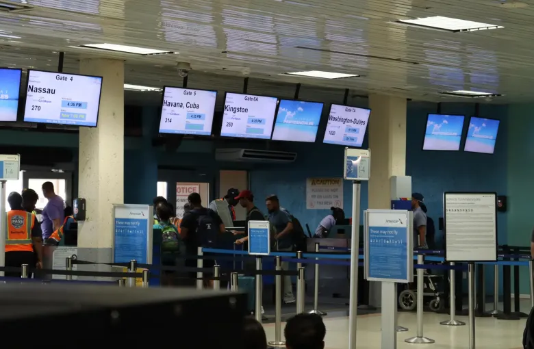 Passengers waiting at the departure gates of Providenciales International Airport, under boards listing flights.