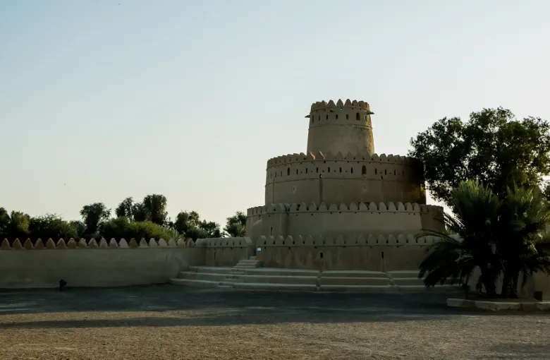 The round crenellated tower and outer wall of Al Jahili Fort in Al Ain, with palms alongside