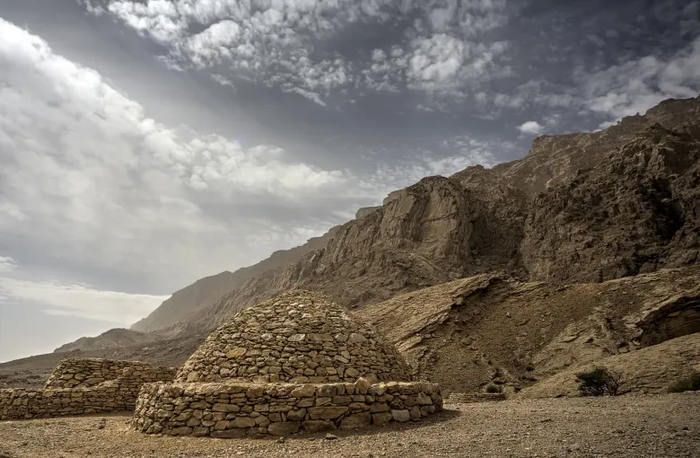 A drystone beehive tomb on a bare rocky slope below the Jebel Hafit ridge