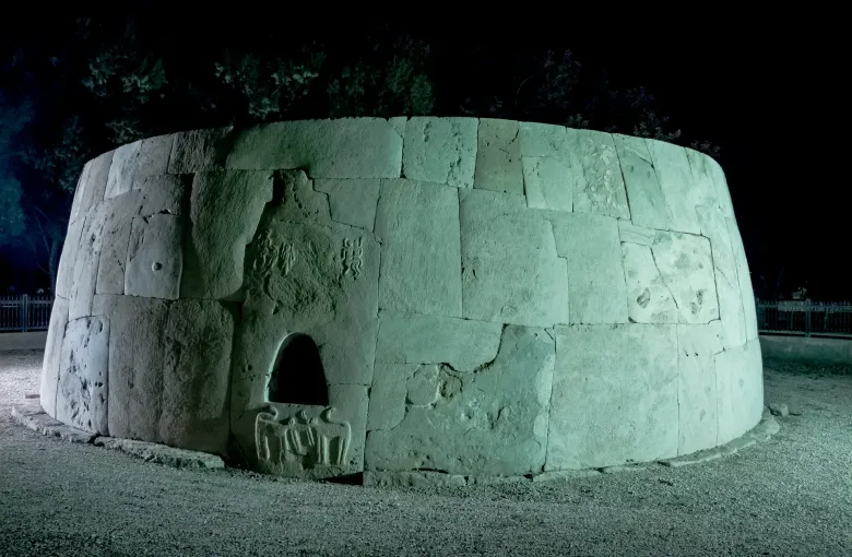 The drystone Hili Grand Tomb, a circular Bronze Age burial structure with a low carved entrance, lit at night