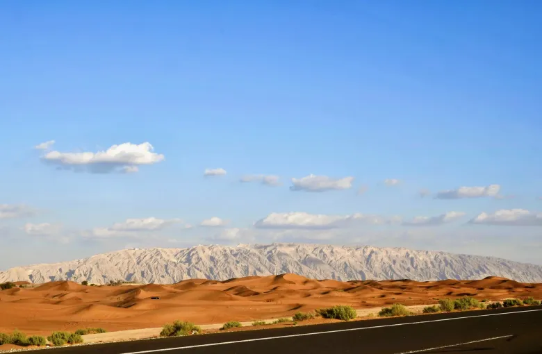 Red dunes in the foreground with the long limestone ridge of Jebel Hafit rising behind