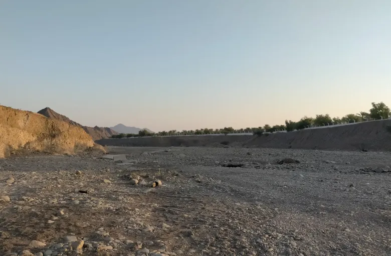 The dry boulder bed and scrub of the lower course of Wadi Wurayah, enclosed by bare mountain slopes