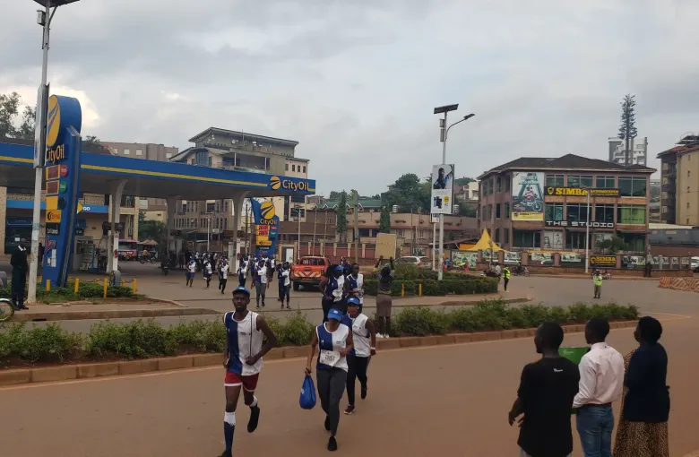 People walking past a filling station and shopfronts on a wide street in Kampala, Uganda.