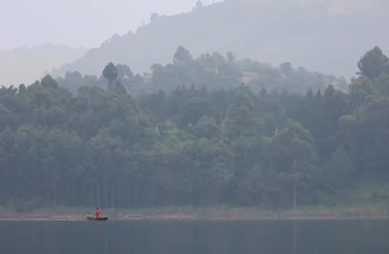 Terraced hills falling to the still water of Lake Bunyonyi in southwest Uganda, with a small boat on the lake.