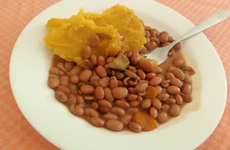A plate of mashed green banana with beans and a fork, a everyday Ugandan meal.