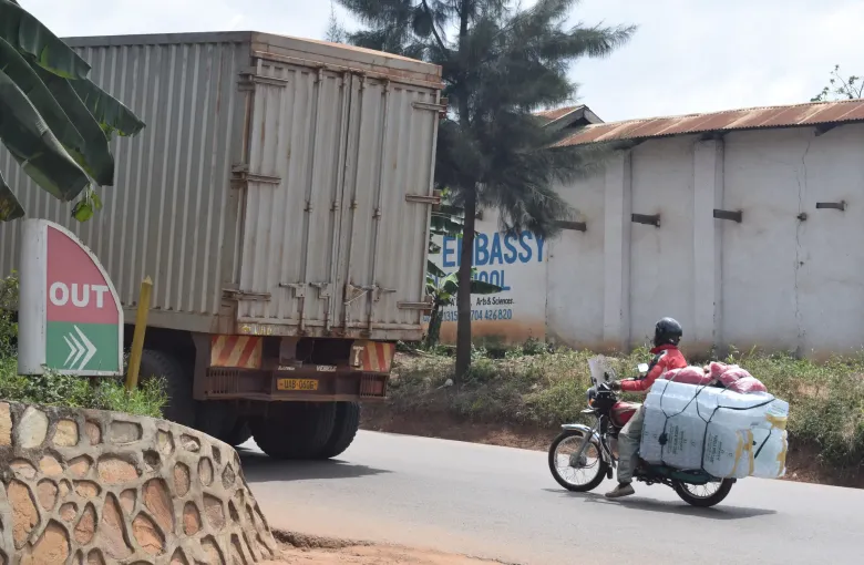 A heavy truck and a motorcycle carrying a large bundled load sharing a roadside in Uganda.