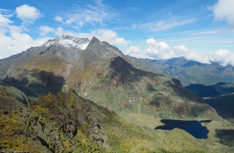 A snow and ice capped peak rising above moorland and a dark tarn in the Rwenzori Mountains, Uganda.