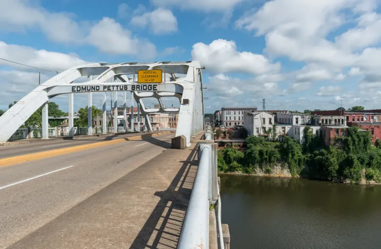 A steel arch bridge carrying its name across the span, crossing the river toward the buildings of downtown Selma.