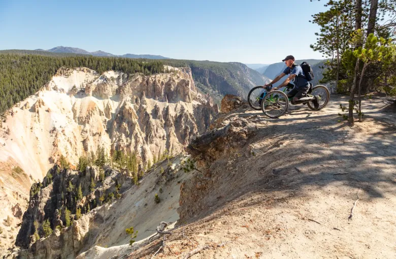 A visitor in an off road wheelchair on a dirt trail at the rim of a pale rock canyon, looking out over the drop.