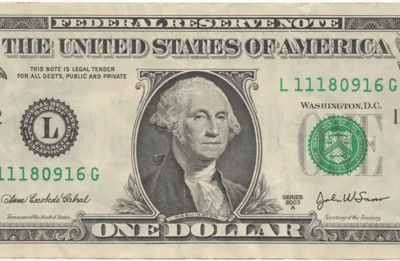 The face of a United States one dollar bill, showing the portrait, the Treasury seal and the green serial numbers.