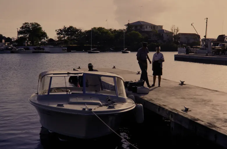 Two park staff stepping onto the dock at Cruz Bay beside a small boat, in a mid century photograph.