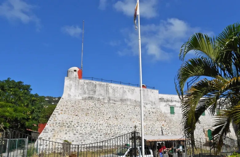 The whitewashed stone bastion wall of Fort Christian at Charlotte Amalie, palms and a flagpole above it.