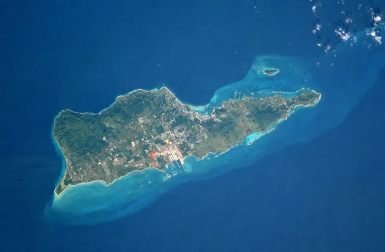 St Croix photographed from orbit, the whole island ringed by the pale shallows of its reef shelf.